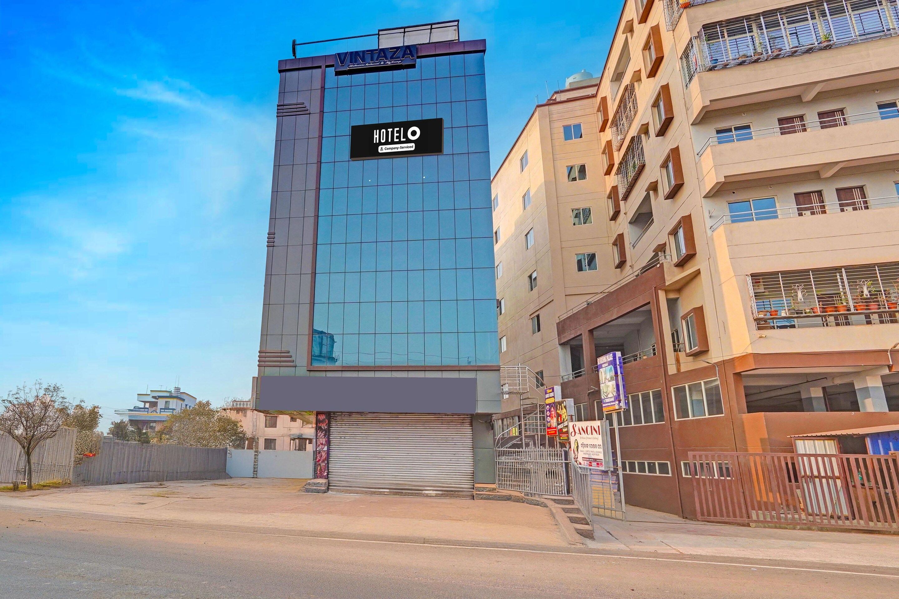A modern hotel with a prominent sign, a glass facade, and a gated entrance.