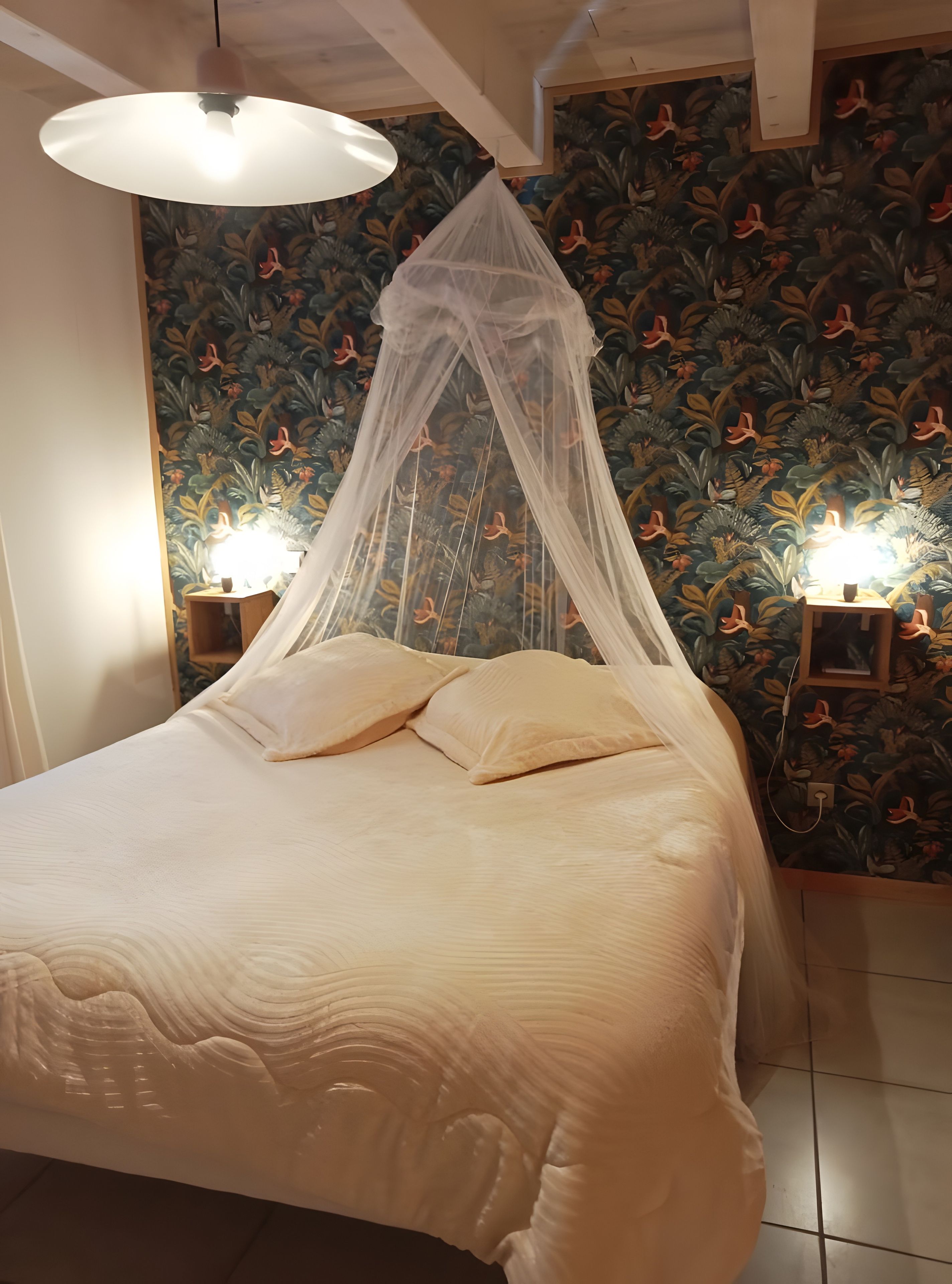 Een bed met hemelbed, twee bedlampjes en bloemenbehang.