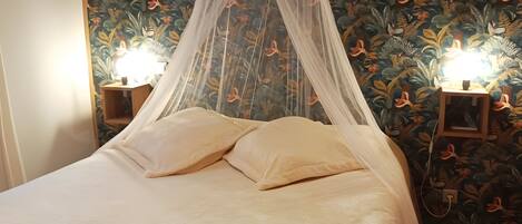 Een bed met hemelbed, twee bedlampjes en bloemenbehang.