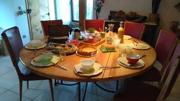 Ein Esstisch ist reichhaltig mit Geschirr, Gläsern und Besteck gedeckt und von Stühlen umgeben.
