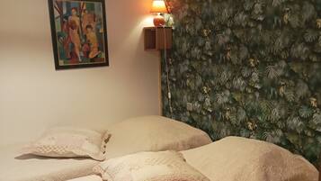 Ein Zimmer mit zwei Betten, einer Wandlampe, einem gerahmten Gemälde und einer strukturierten Tapete.