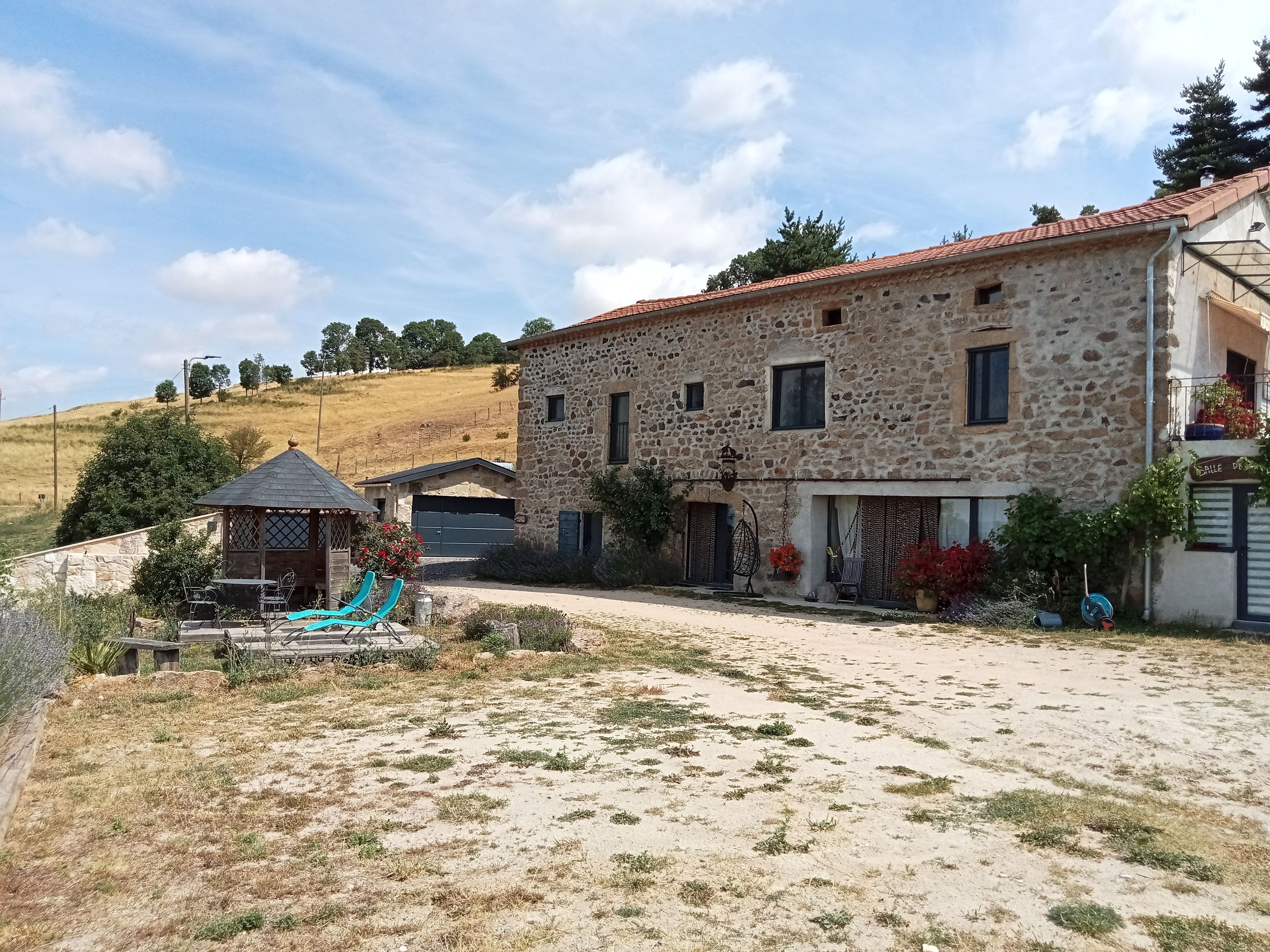 A stone building with a tiled roof, a covered outdoor seating area, and a paved driveway.