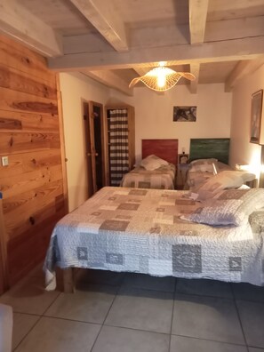 Una camera da letto con pavimento in legno, un letto con copriletto a fantasia, una testiera in legno, una lampada a sospensione e una porta con tenda a righe.