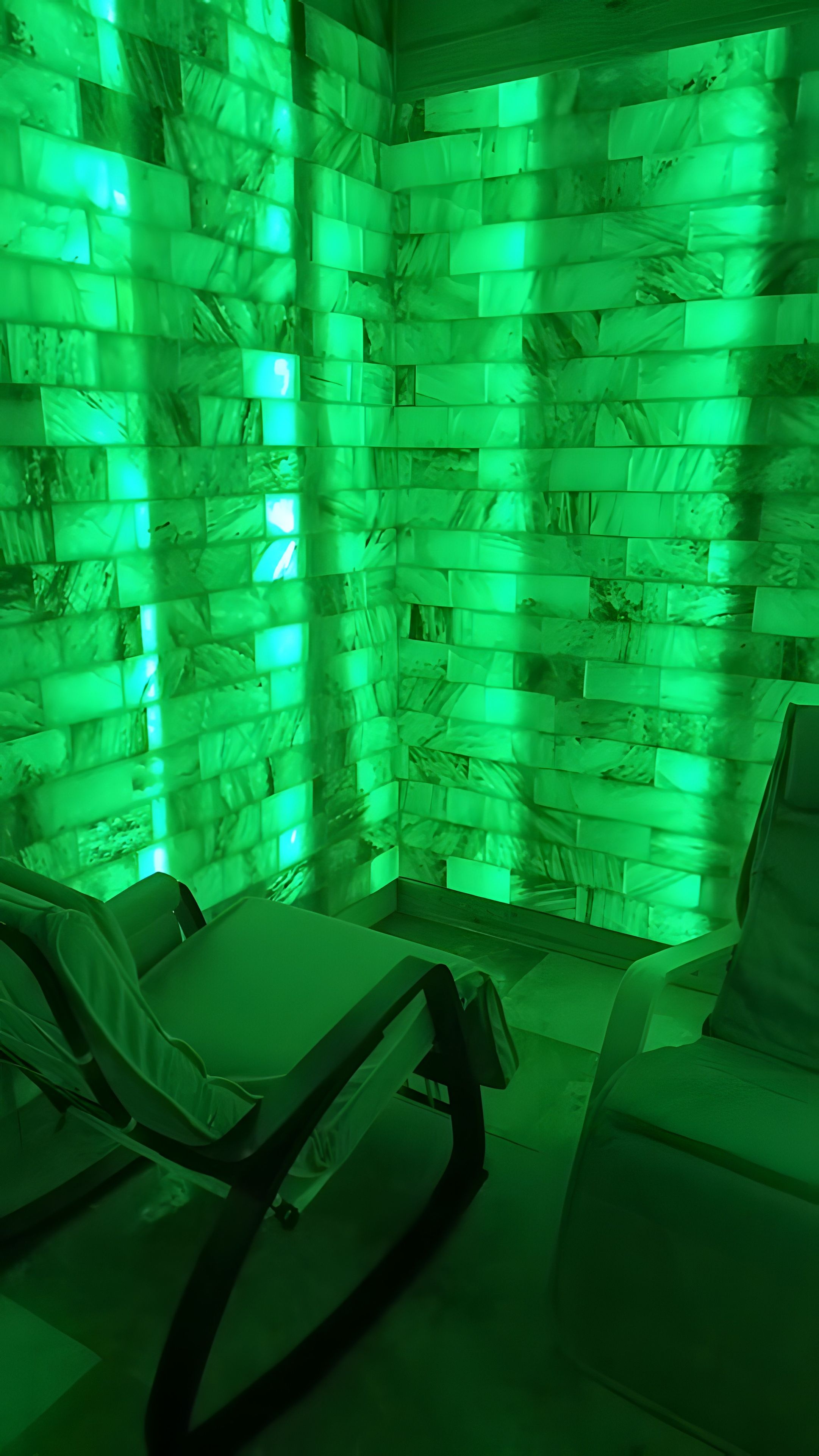 Une pièce avec un mur éclairé en vert, deux fauteuils inclinables et une petite table.