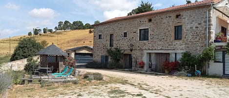A stone building with a tiled roof, a covered outdoor seating area, and a paved driveway.