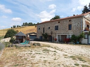 Un edificio in pietra con tetto a tegole, una zona relax all'aperto coperta e un vialetto lastricato.
