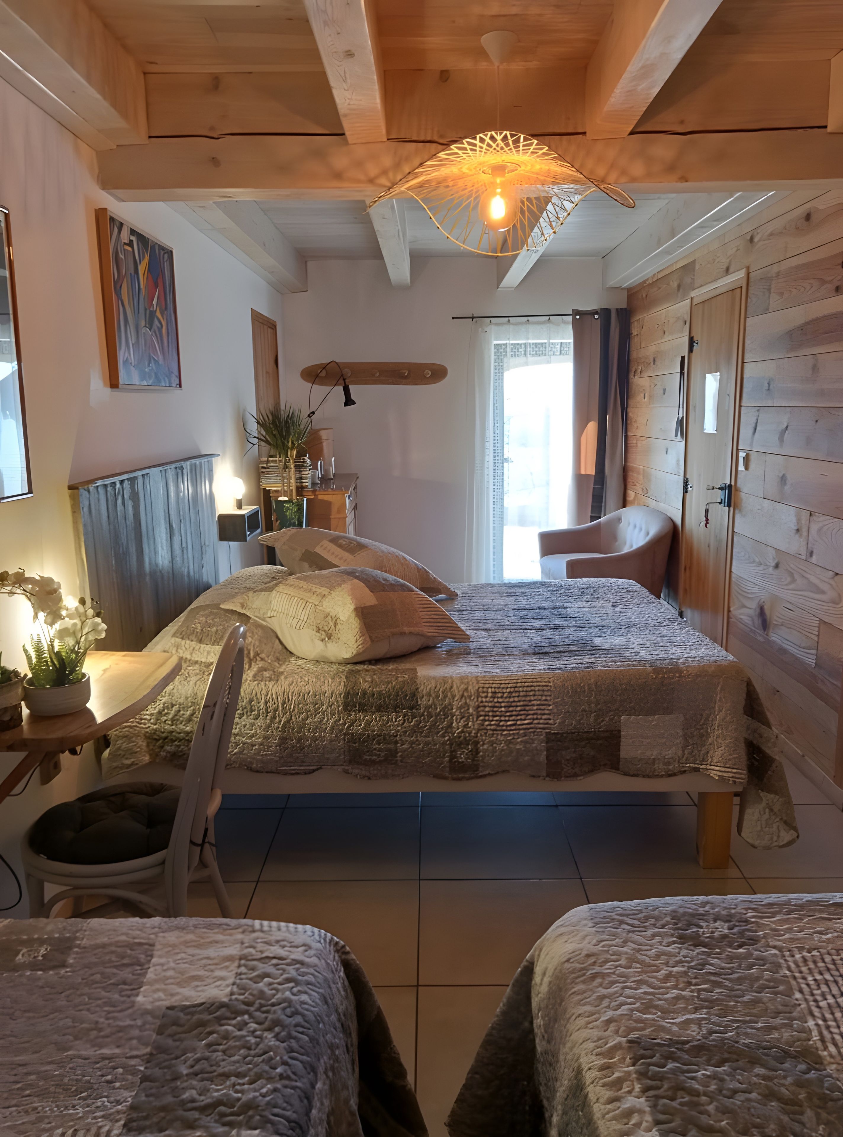 A bedroom with a large bed, a chair, a bedside table, and a hanging light fixture.