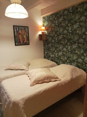 A room with two beds, a wall-mounted lamp, a framed painting, and a textured wallpaper.
