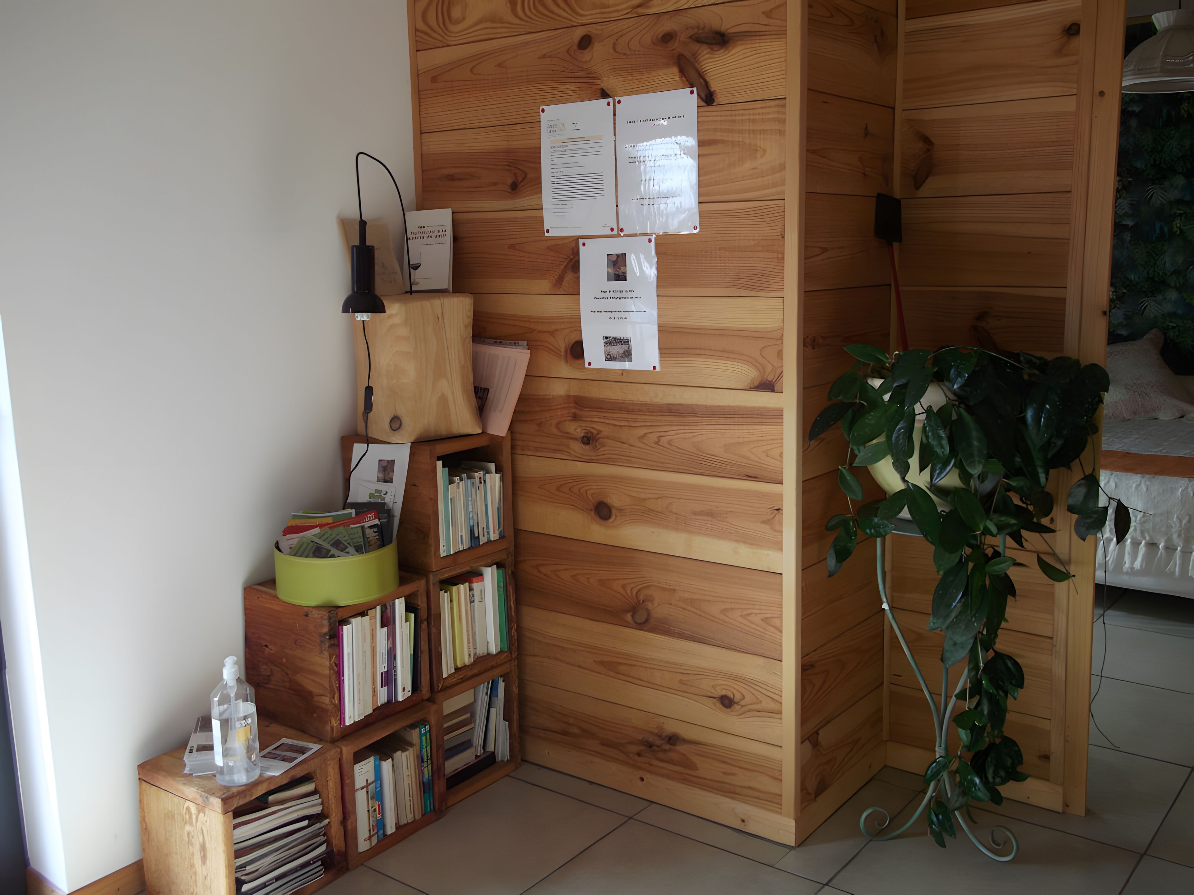 Une bibliothèque en bois contenant divers livres et documents, une poubelle verte, une bouteille d’eau en plastique transparente et une plante en pot.
