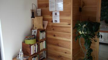 A wooden bookshelf with various books and papers, a green trash bin, a clear plastic water bottle, and a potted plant.