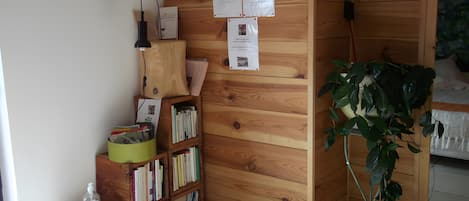 Une bibliothèque en bois contenant divers livres et documents, une poubelle verte, une bouteille d’eau en plastique transparente et une plante en pot.