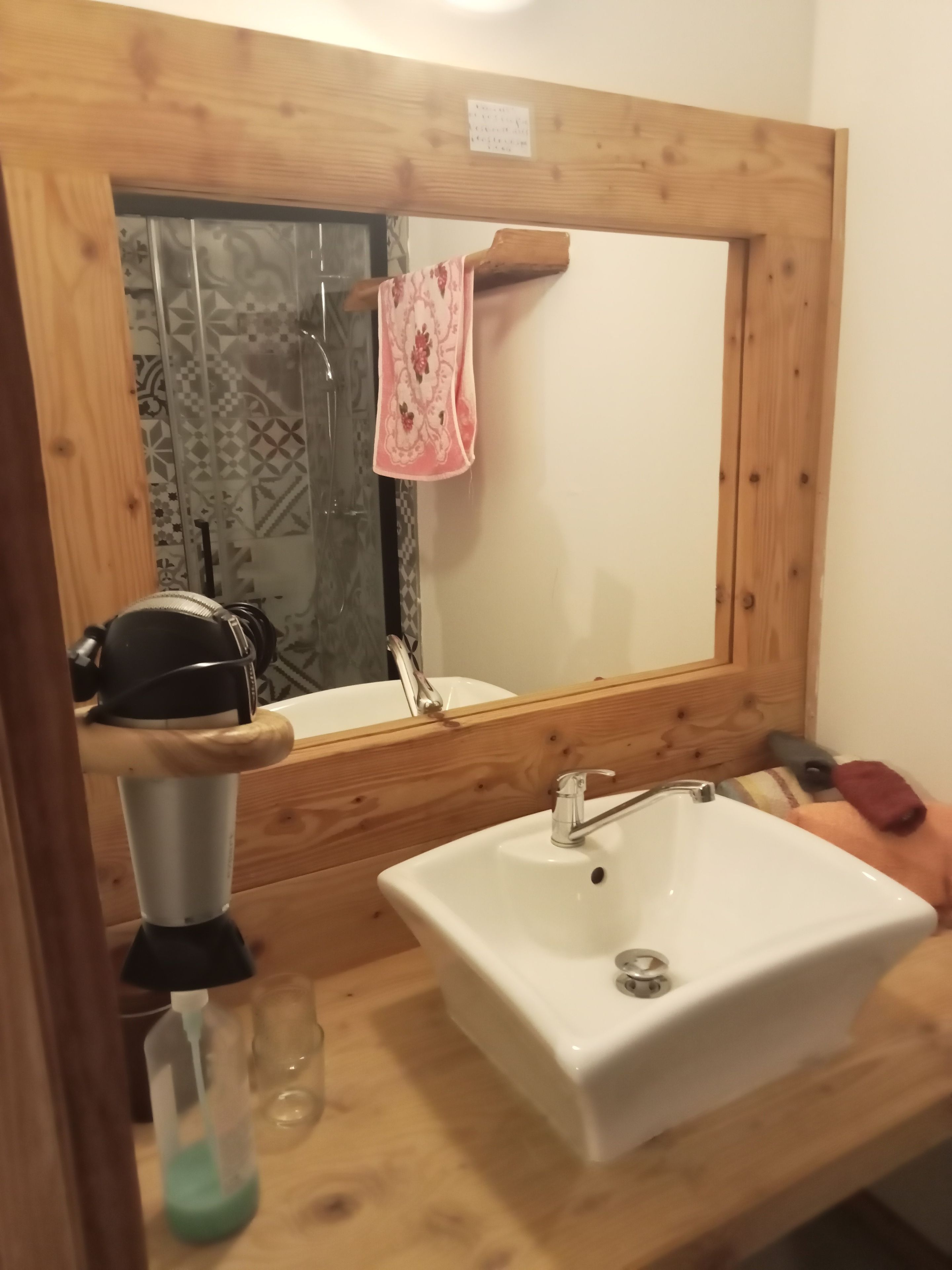A bathroom with a wooden-framed mirror, a white sink, and a shower area.