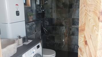 Een kleine badkamer met een wasmachine, toilet en douche.