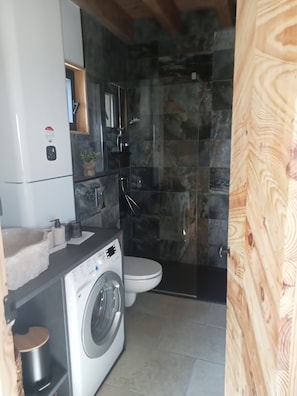 Een kleine badkamer met een wasmachine, toilet en douche.