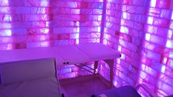 Ein Zimmer mit einer Massageliege, einem Massagesessel und einer Wand mit Struktur.