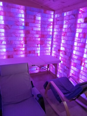 Een kamer met een massagetafel, een massagestoel en een wand met een structuur.