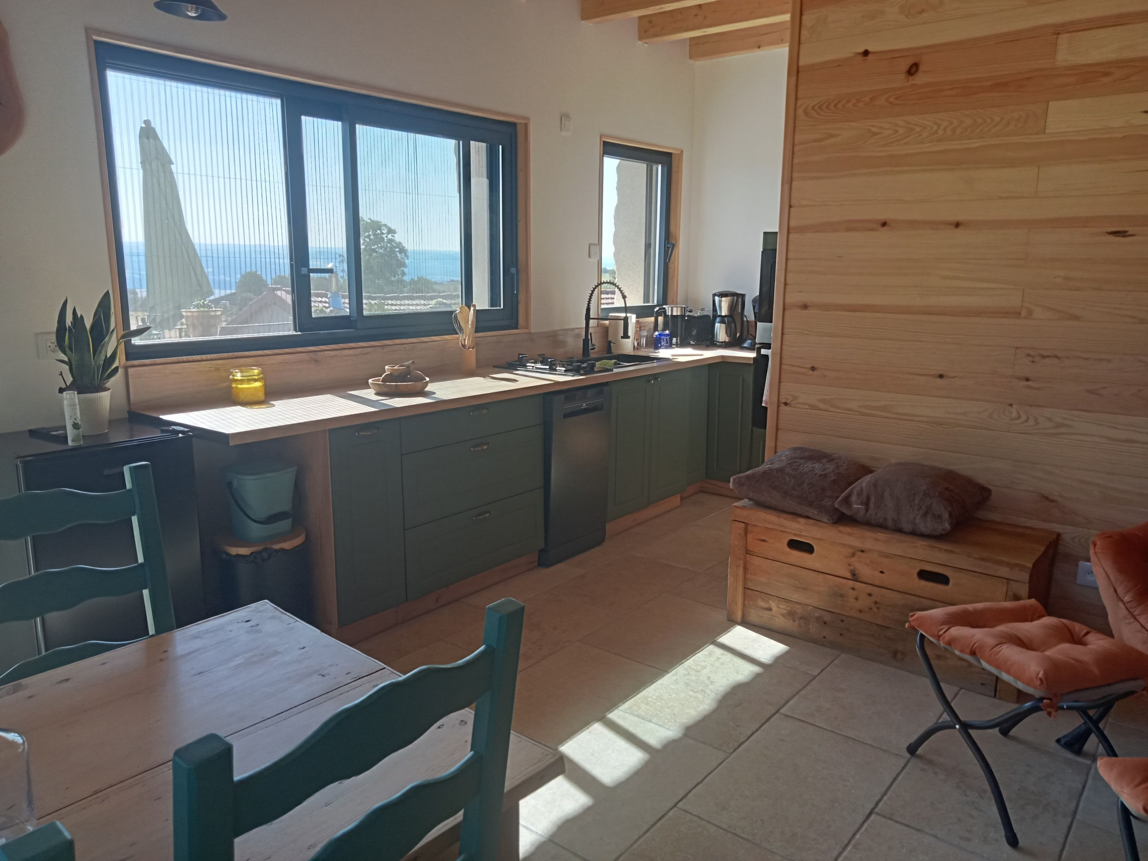Una cocina con un ventanal grande, armarios de madera, un fregadero y un comedor con sillas.