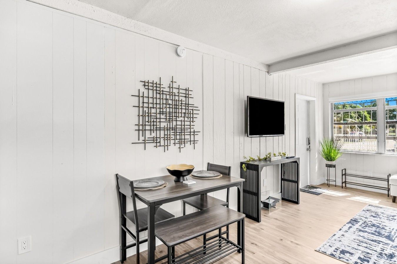 A dining area with a table, chairs, a bowl, and a TV mounted on the wall.
