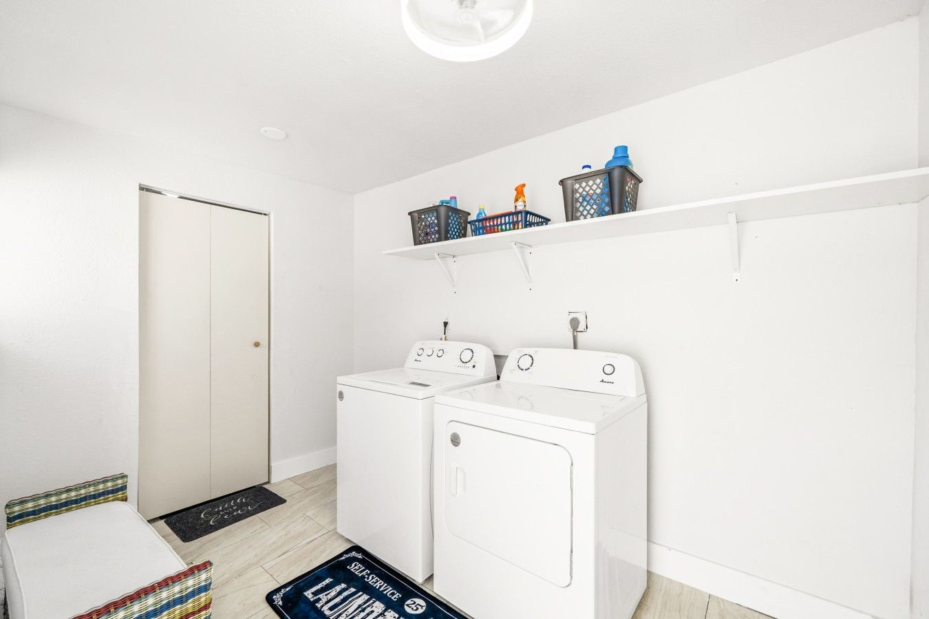 A laundry room with two white washing machines, a shelf with laundry supplies, and a door.
