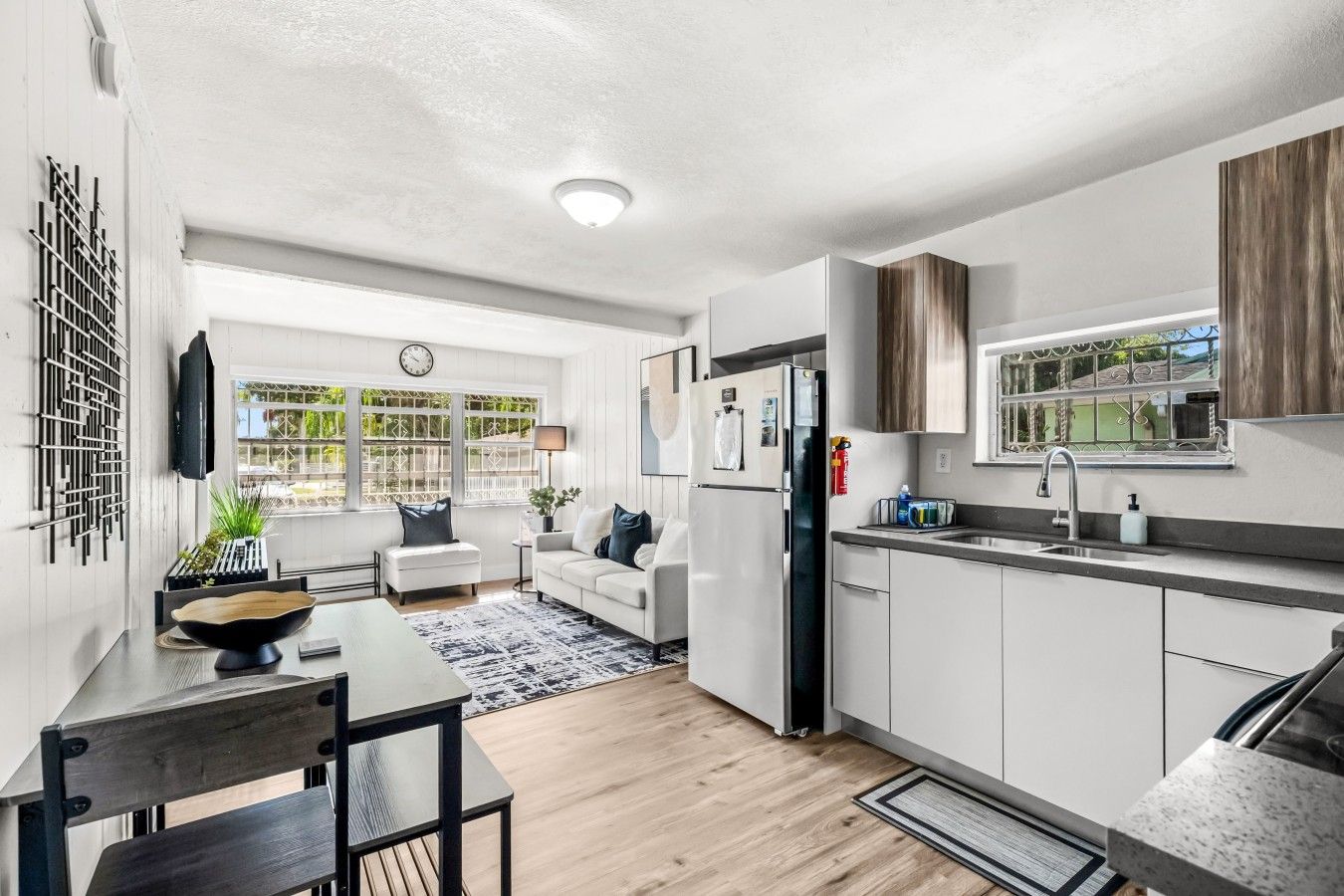 A modern kitchen with white cabinets, a built-in refrigerator, and a window overlooking a garden.