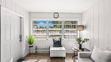 Ein Zimmer mit weißer Tür, einer Bank, einem Sofa, einer Lampe und einem Fenster mit Blick nach draußen.