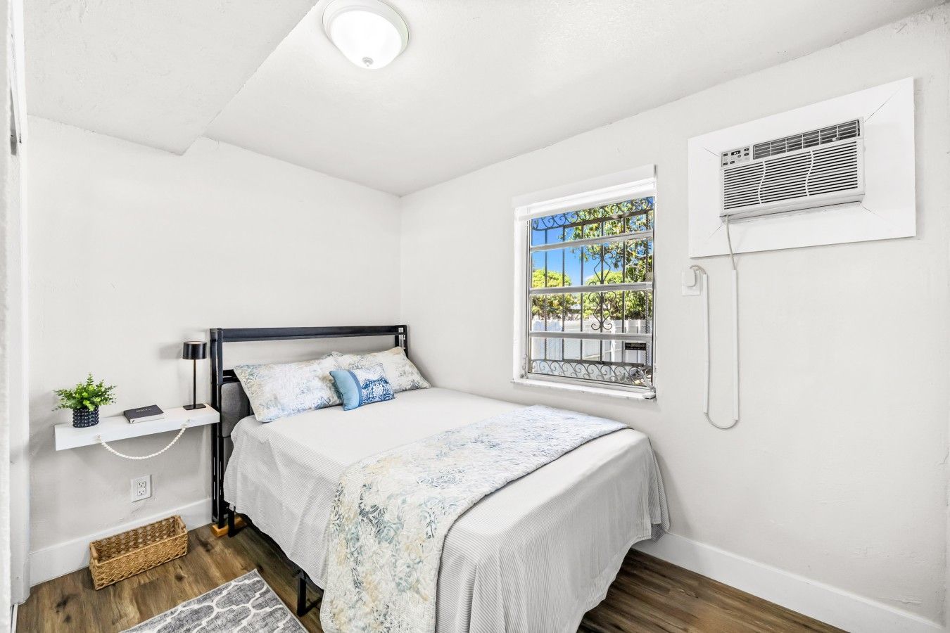 A bedroom with a bed, bedside table, lamp, and a window with a view.