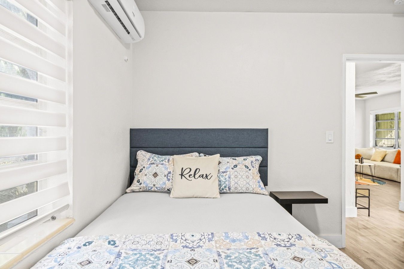 A bedroom with a bed, a bedside table, a nightstand, and a window with blinds.