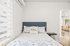 A bedroom with a bed, a bedside table, a nightstand, and a window with blinds.