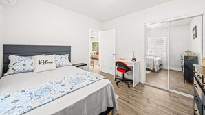 Een slaapkamer met een bed, een bureau, een stoel, een kledingkast en een spiegel.