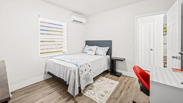 Een slaapkamer met een bed, nachtkastje en een rode stoel.