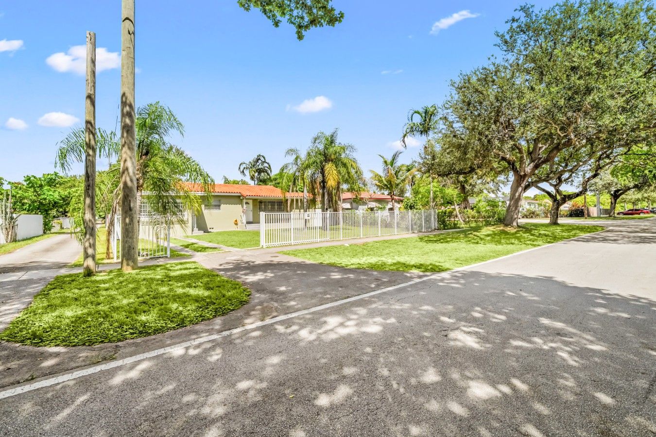 A residential street with a gated entrance, a house with a red roof, and trees lining the road.