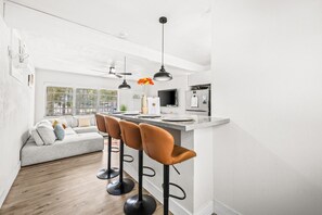 Une cuisine moderne avec un coin bar, un canapé gris et une grande fenêtre.
