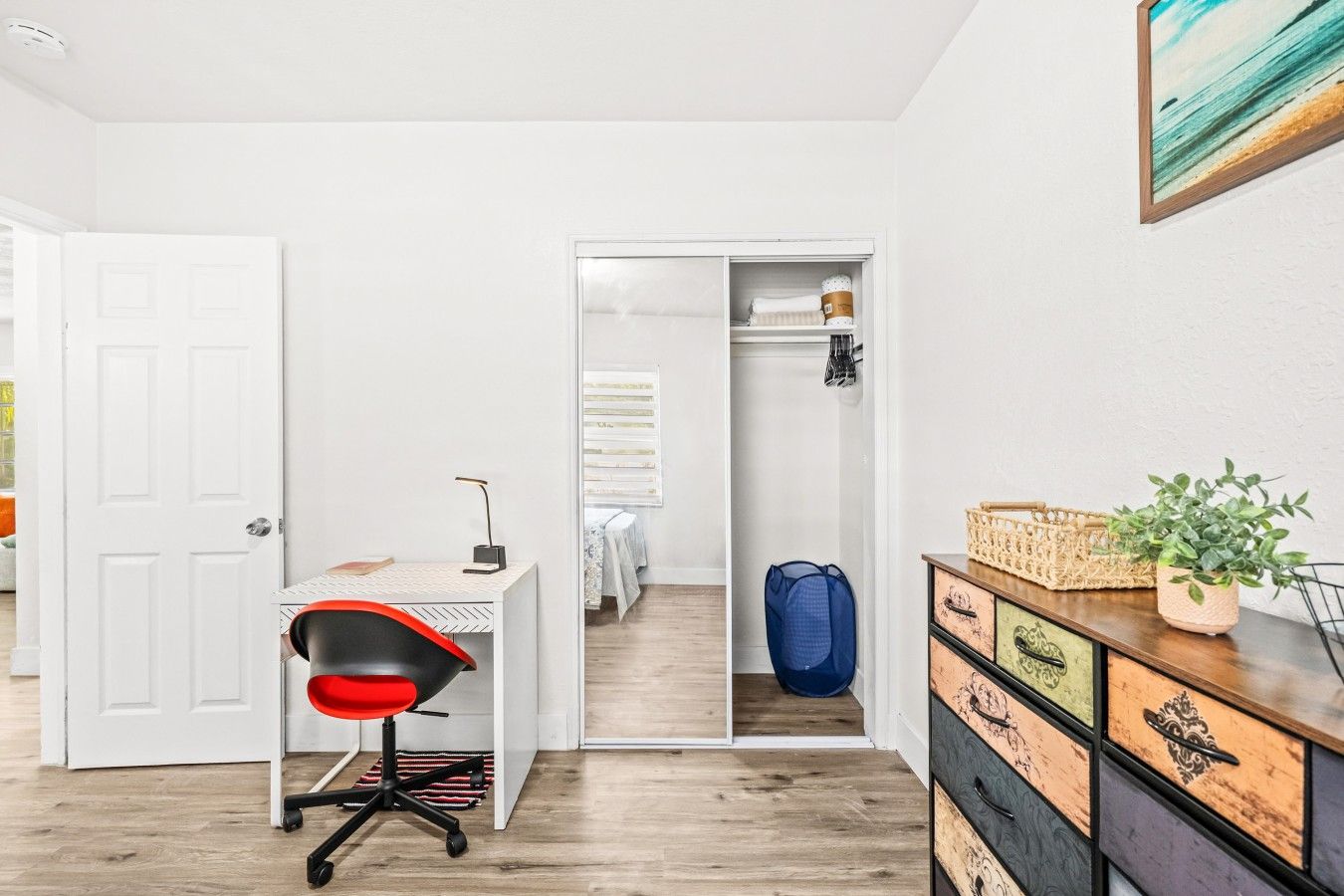 A room with a desk, chair, wardrobe, and a plant.