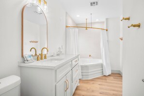 A modern bathroom with a white vanity, gold fixtures, a large mirror, and a shower area. - Tan Lines & Fine Wines | Gorgeous Home + Walk to Beach! (Port Aransas)