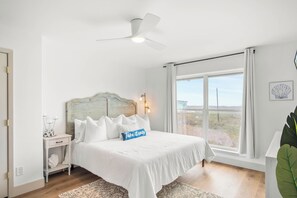 A bedroom with a bed, bedside table, nightstand, and a window with a view. - Tan Lines & Fine Wines | Gorgeous Home + Walk to Beach! (Port Aransas)
