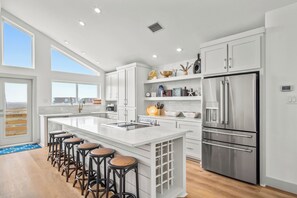 Une cuisine moderne dotée d’un grand îlot central, d’appareils électroménagers en acier inoxydable et offrant une vue sur l’extérieur.