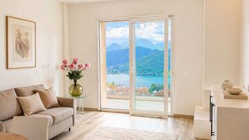 Ein modernes Wohnzimmer mit einer Couch, einem Esstisch und Blick auf eine Berglandschaft durch große Glasfenster.