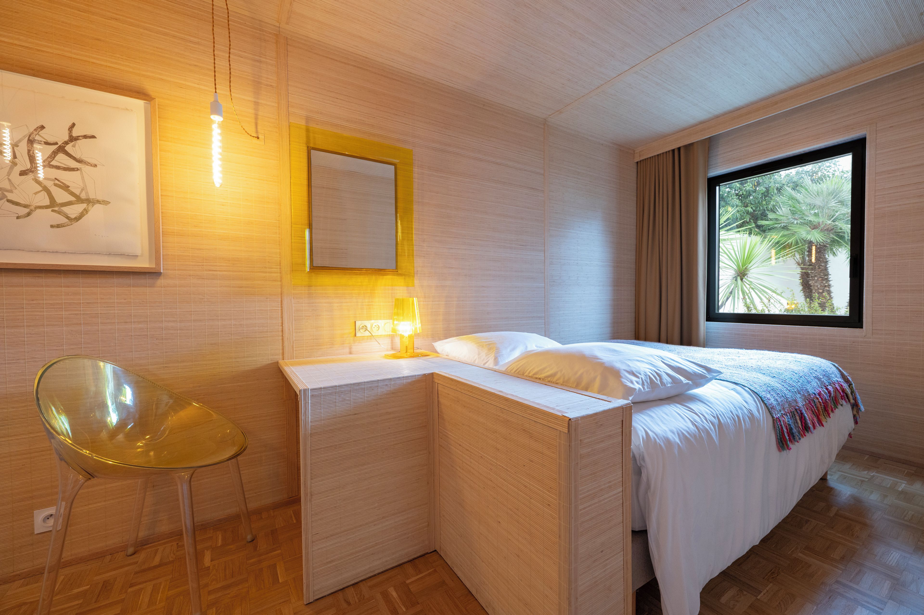 Ein modernes Schlafzimmer mit Bett, Nachttisch, Lampe, Stuhl und einem Kunstwerk an der Wand.