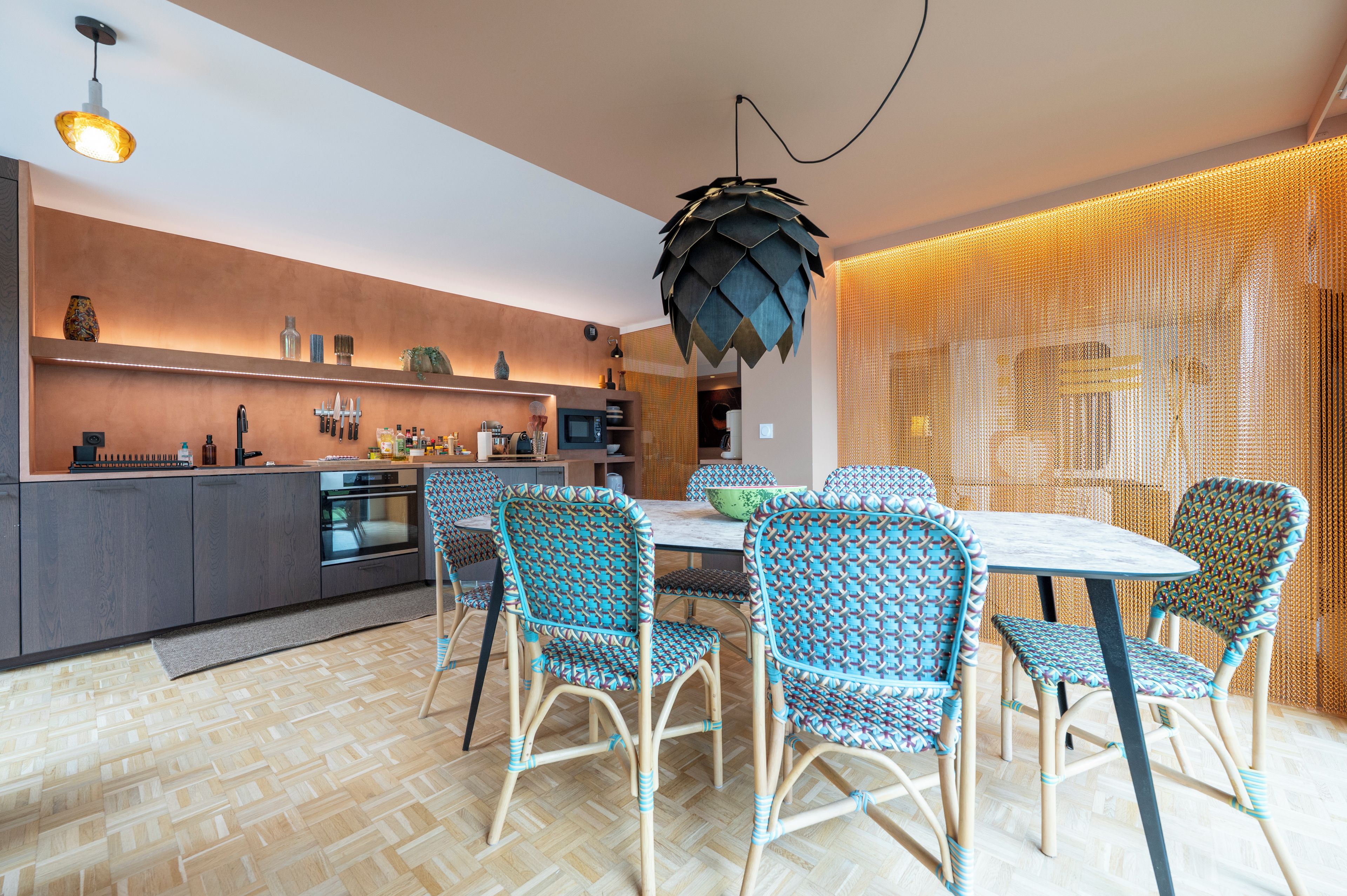 Une cuisine moderne avec un coin repas, comprenant un îlot central, des appareils électroménagers intégrés et un luminaire au plafond au design original.
