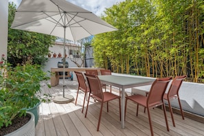 Eine Außenpatio mit Tisch und Stühlen, einem großen Sonnenschirm und einem Bambuszaun.