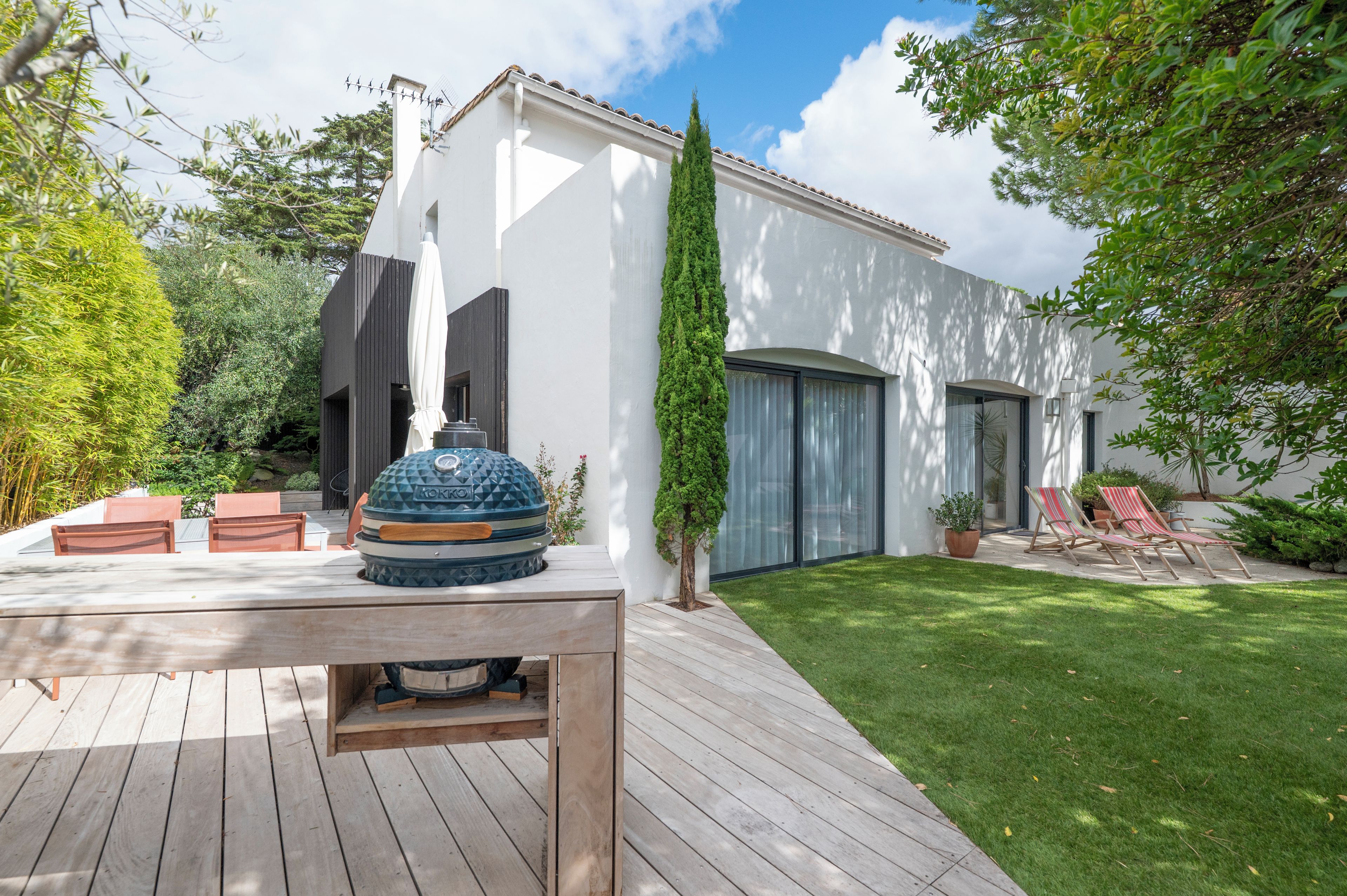 A modern outdoor patio with a barbecue grill, wooden deck, and a well-maintained lawn.
