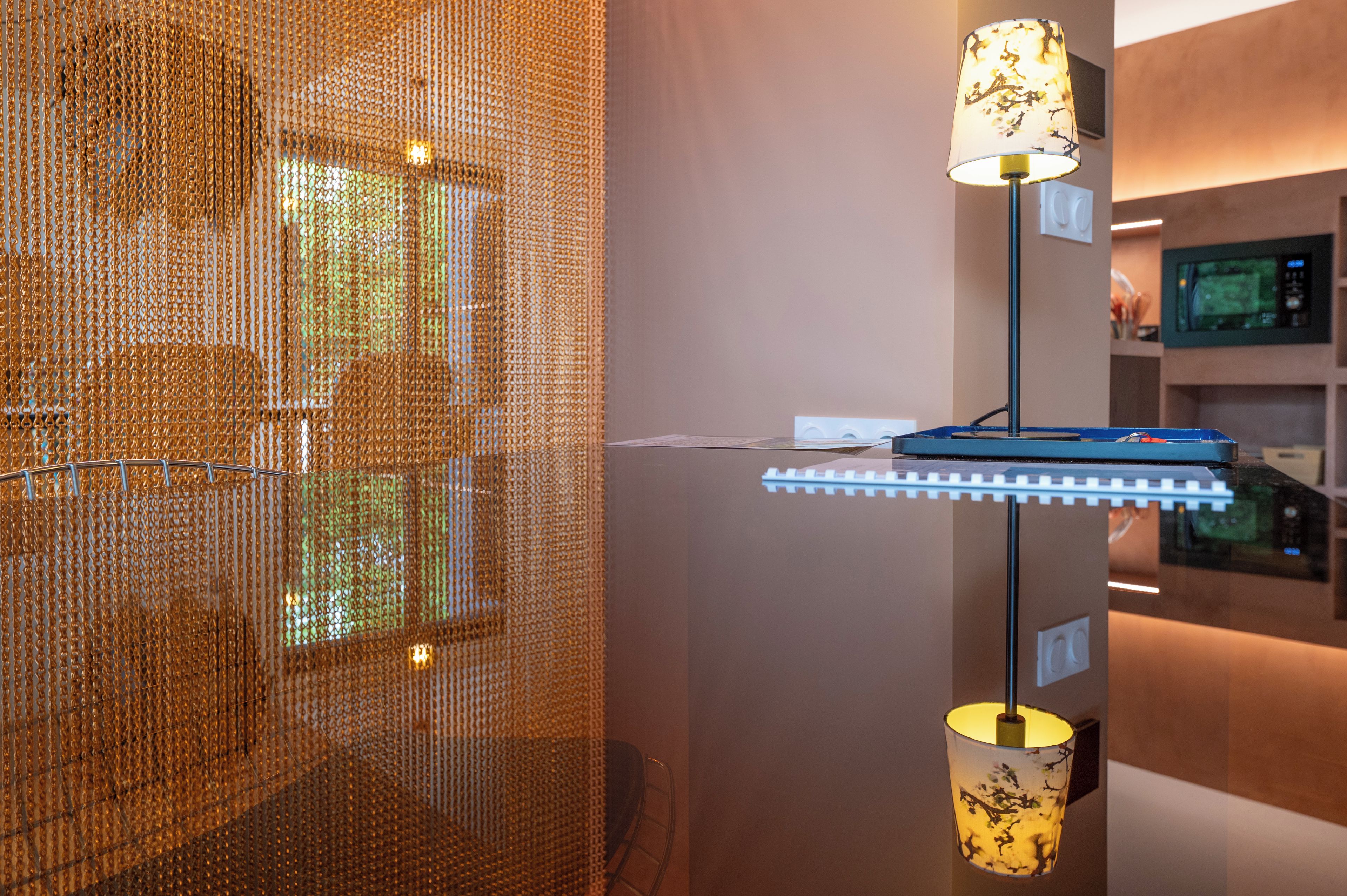 A modern interior with a metallic mesh partition, a blue desk with a lamp, and a television mounted on the wall.