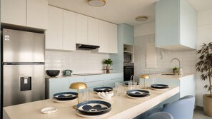 Eine moderne Küche mit weißen Schränken, einem Edelstahlkühlschrank und einer hellblauen Arbeitsplatte.