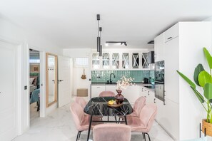 A modern kitchen with white cabinets, a marble-top dining table, and pink chairs. - Marbella Playa Real | Pool & Sea View | 2 Bedrooms (Marbella)
