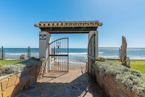 A stone pathway leading to a gated entrance with a view of the ocean. - Marbella Playa Real | Pool & Sea View | 2 Bedrooms (Marbella)