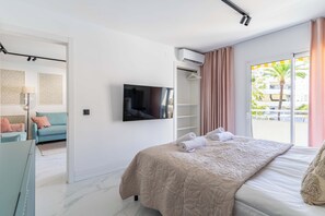A modern hotel room with a bed, a TV, a wardrobe, and a balcony with a view of palm trees. - Marbella Playa Real | Pool & Sea View | 2 Bedrooms (Marbella)