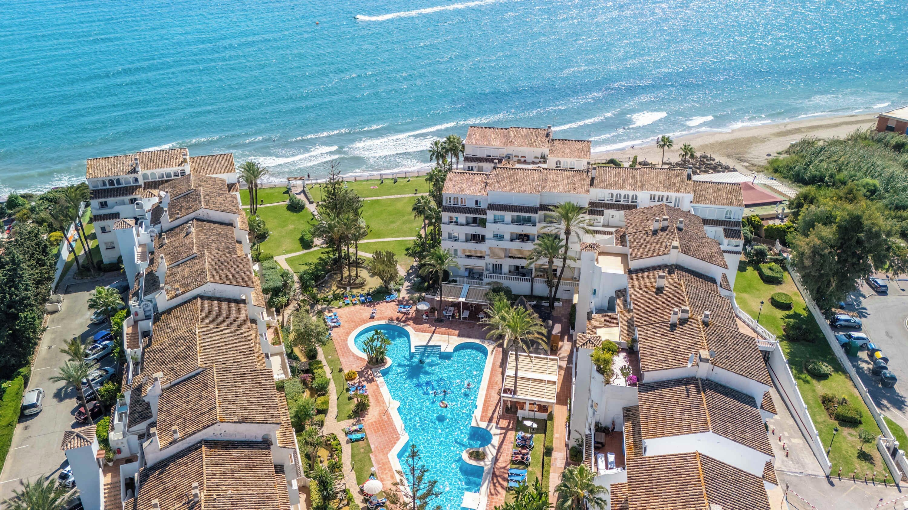 A resort with a central swimming pool, beachfront views, and terracotta-roofed buildings.