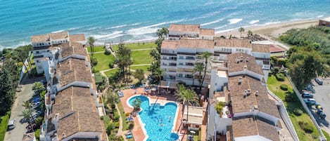 A resort with a central swimming pool, beachfront views, and terracotta-roofed buildings.