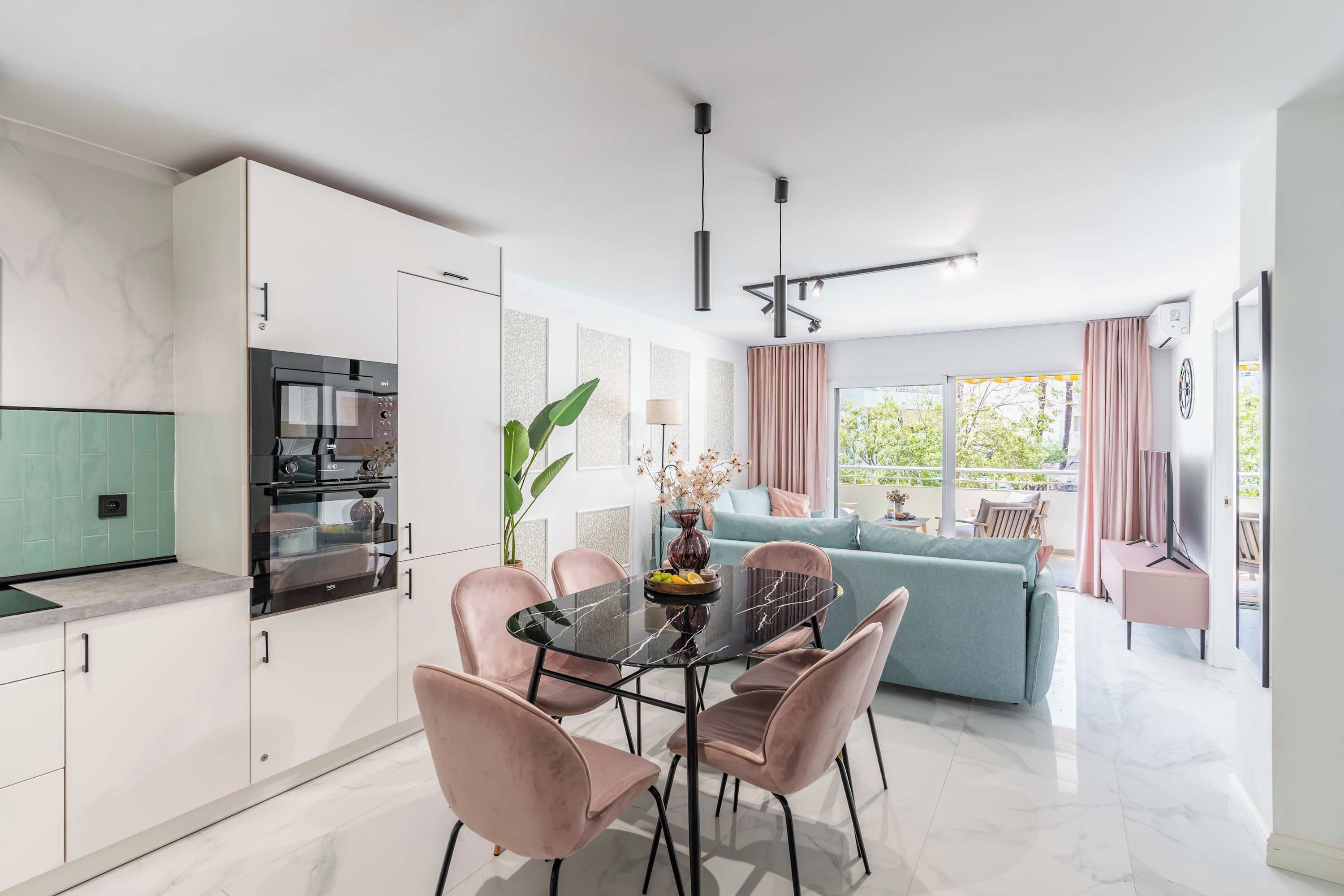 A modern kitchen with a built-in oven and a dining area with a marble table and pink chairs.