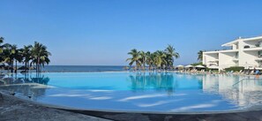 A resort pool with clear blue water, surrounded by palm trees and a white building with balconies. - Fabulous Presidential Suite with AC and full kitchen  in sunny Nuevo Nayarit (Nuevo Nayarit)
